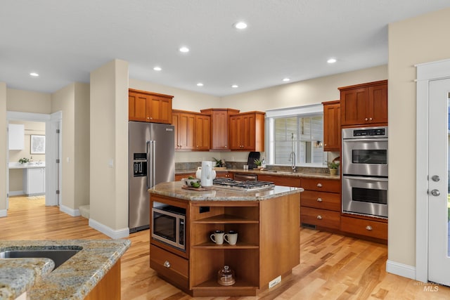 kitchen featuring stainless steel appliances, sink, light stone counters, light hardwood / wood-style flooring, and a center island