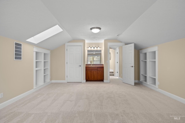 bonus room featuring built in shelves, light carpet, lofted ceiling with skylight, and sink