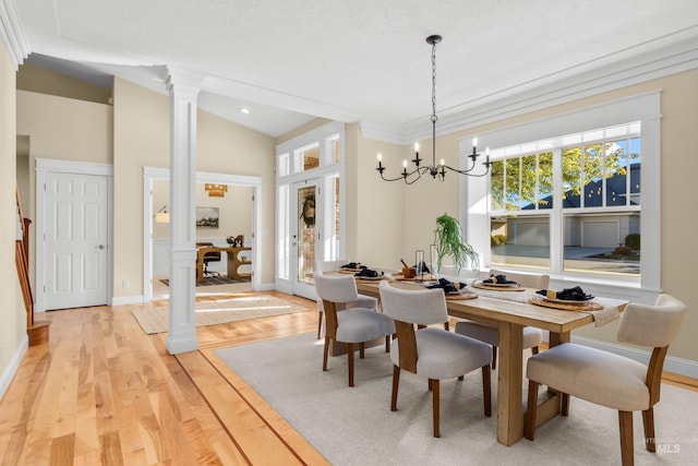 dining space featuring light hardwood / wood-style floors, vaulted ceiling, an inviting chandelier, decorative columns, and ornamental molding