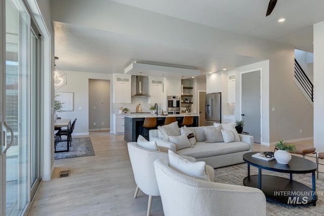 living area with recessed lighting, visible vents, baseboards, light wood-style floors, and stairway