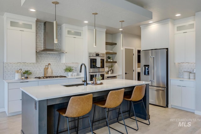 kitchen featuring stainless steel appliances, a breakfast bar, a sink, wall chimney range hood, and open shelves