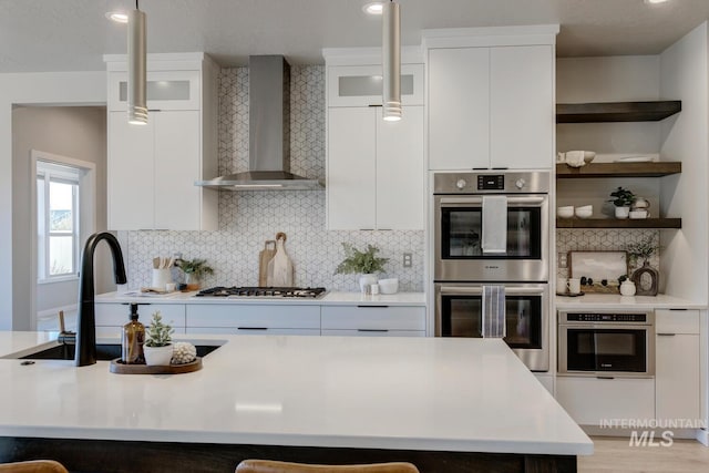 kitchen with gas stovetop, light countertops, double oven, white cabinets, and wall chimney exhaust hood