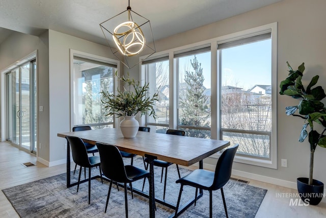 dining area with light wood-type flooring, visible vents, baseboards, and an inviting chandelier