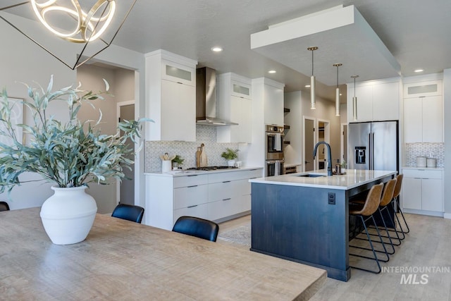 kitchen featuring white cabinets, a breakfast bar, stainless steel appliances, wall chimney range hood, and a sink