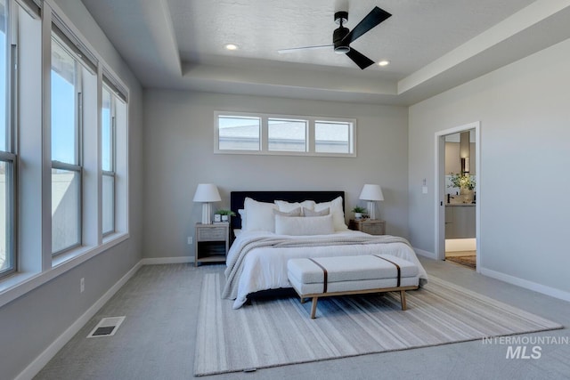 bedroom featuring a raised ceiling, visible vents, baseboards, and multiple windows