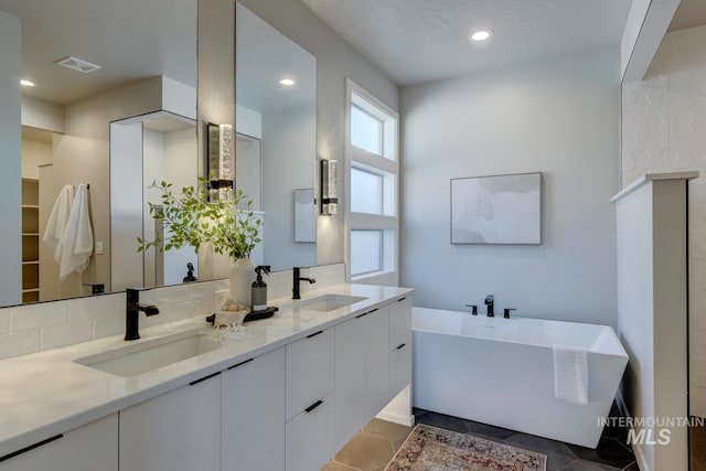 bathroom with double vanity, a soaking tub, visible vents, and a sink