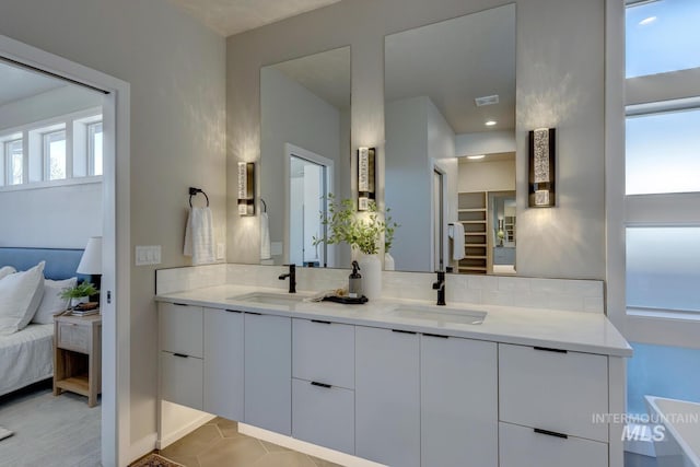 ensuite bathroom featuring double vanity, visible vents, decorative backsplash, and a sink