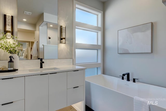 full bathroom with tasteful backsplash, recessed lighting, visible vents, vanity, and a freestanding tub