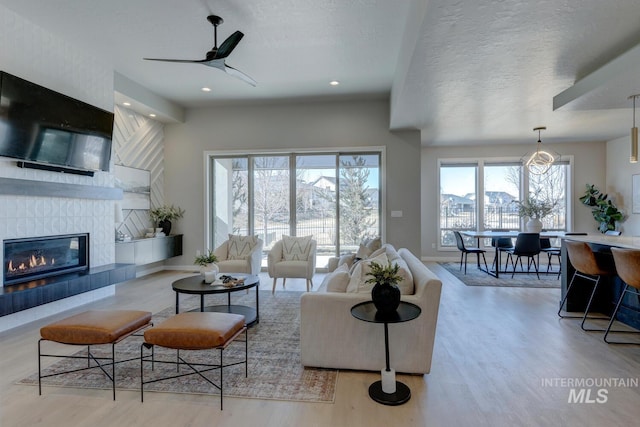 living area with a textured ceiling, recessed lighting, wood finished floors, baseboards, and a tiled fireplace