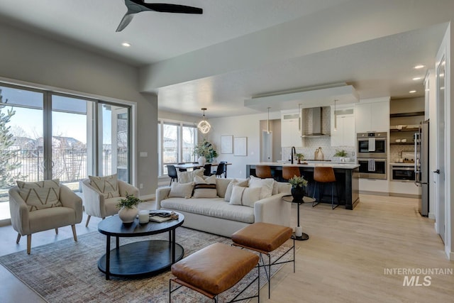 living area with baseboards, light wood-type flooring, a ceiling fan, and recessed lighting