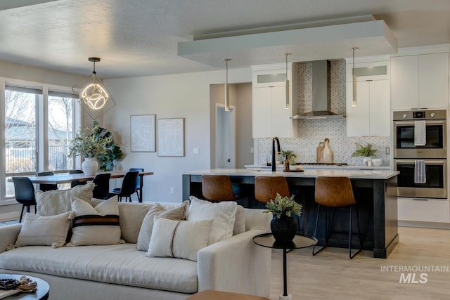 kitchen with double oven, wall chimney range hood, modern cabinets, and light countertops