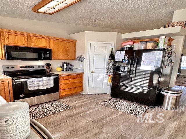 kitchen with light hardwood / wood-style floors, a textured ceiling, and black appliances