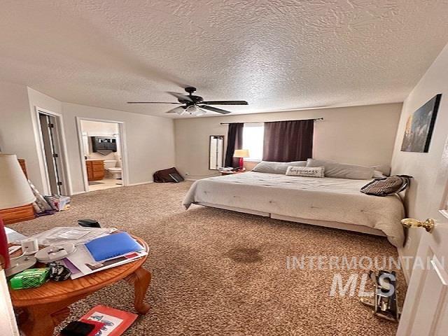 bedroom with ceiling fan, ensuite bathroom, carpet flooring, and a textured ceiling