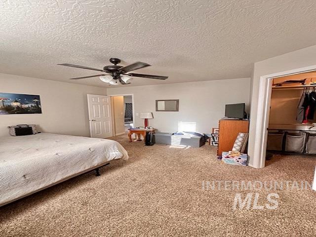 carpeted bedroom with a spacious closet, a textured ceiling, ceiling fan, and a closet