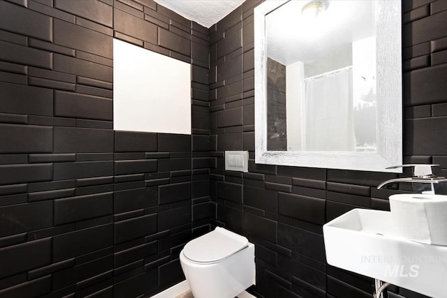 bathroom featuring toilet, sink, and tile walls