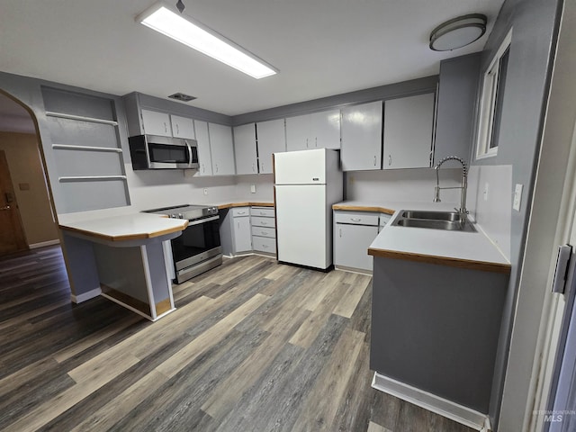 kitchen with wood finished floors, arched walkways, a sink, light countertops, and appliances with stainless steel finishes