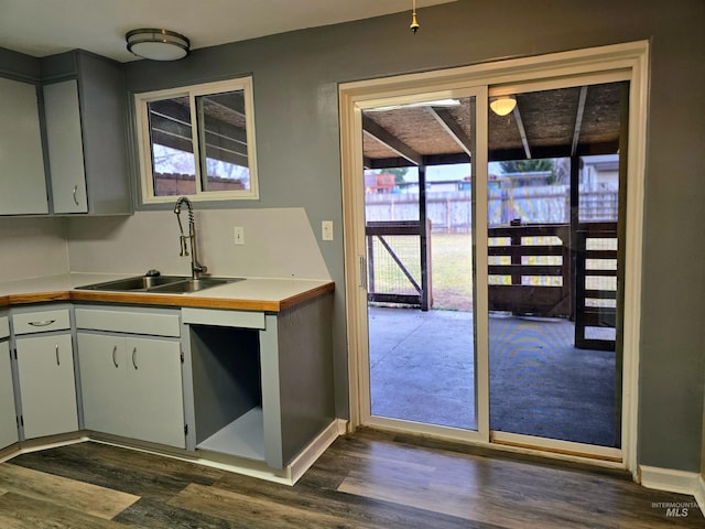 kitchen featuring dark wood finished floors, light countertops, baseboards, and a sink