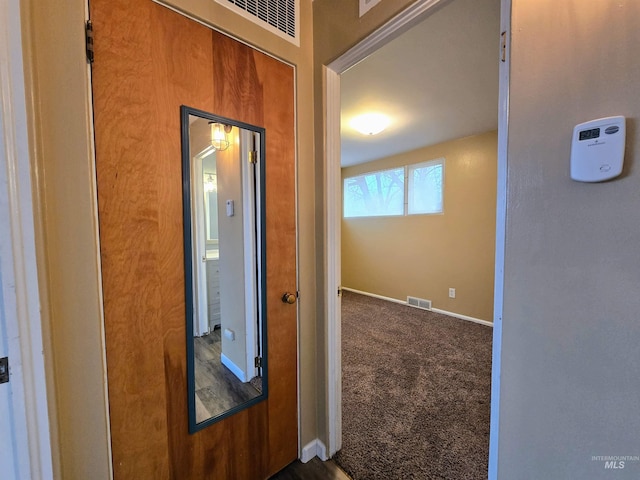 hallway with baseboards, visible vents, and dark carpet