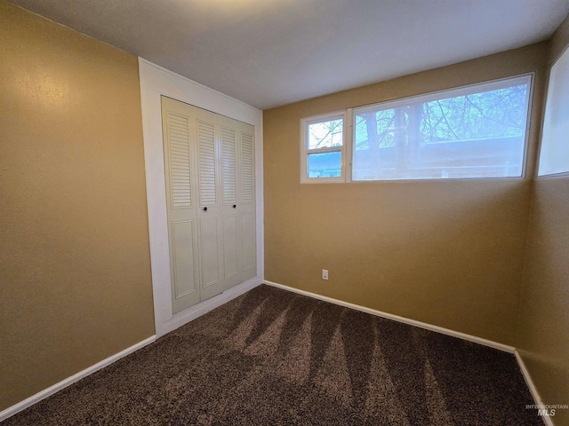 unfurnished bedroom featuring dark colored carpet, a closet, and baseboards