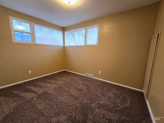 unfurnished room with visible vents, dark carpet, baseboards, and a healthy amount of sunlight