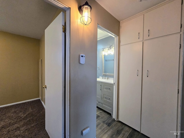 hall featuring a sink, baseboards, and dark wood-style flooring