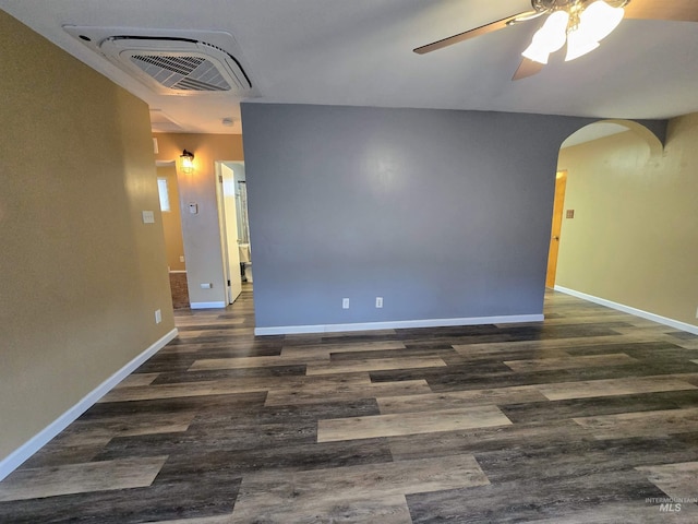 empty room featuring wood finished floors, arched walkways, visible vents, and baseboards