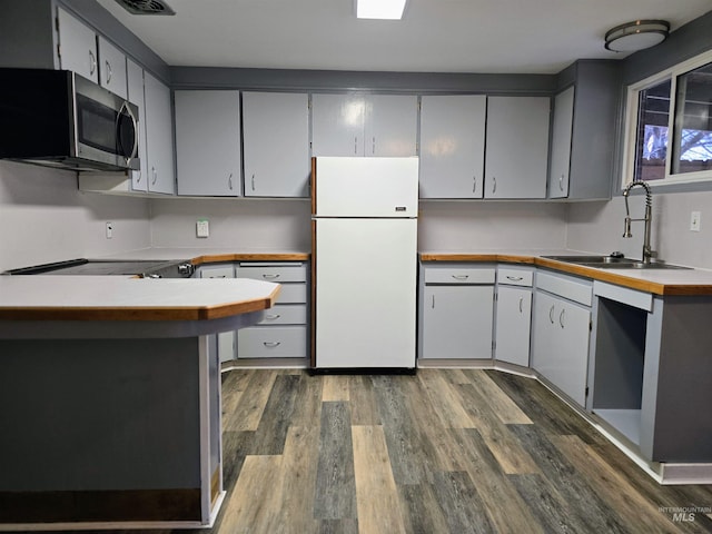 kitchen with stainless steel microwave, dishwashing machine, freestanding refrigerator, dark wood-style floors, and a sink