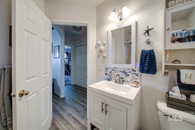 bathroom featuring wood-type flooring, decorative backsplash, walk in shower, vanity, and toilet