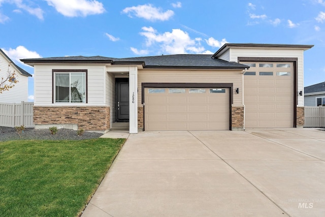 prairie-style house featuring a front yard, stone siding, a garage, fence, and driveway