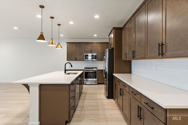 kitchen with a sink, appliances with stainless steel finishes, light wood finished floors, and an island with sink