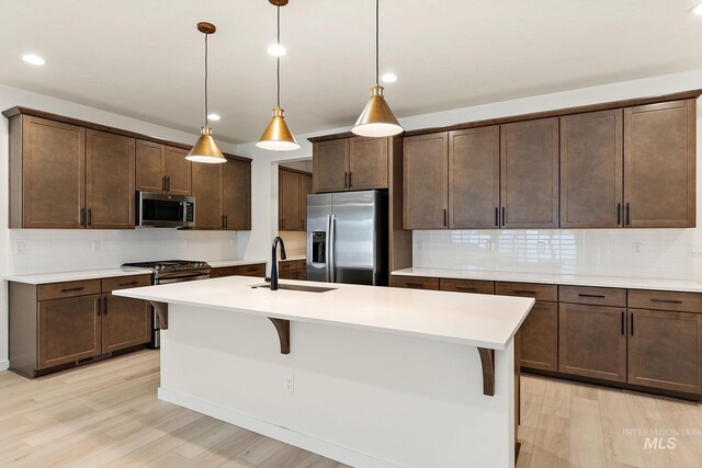 kitchen with light wood-style flooring, a sink, backsplash, and appliances with stainless steel finishes