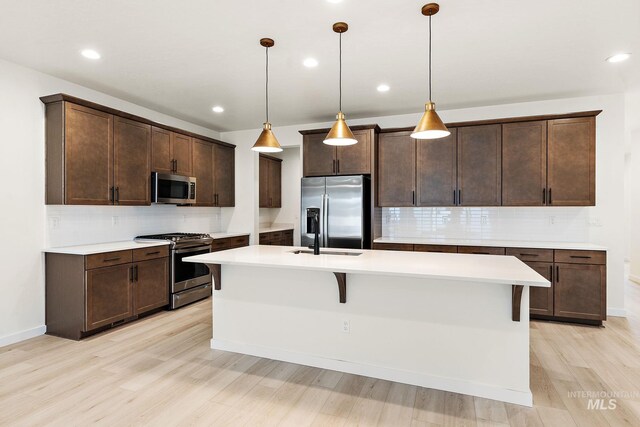 kitchen featuring an island with sink, light countertops, dark brown cabinets, stainless steel appliances, and light wood finished floors