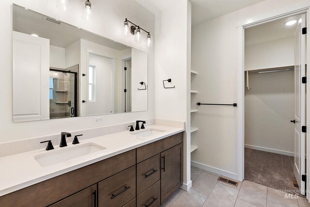 bathroom with a walk in closet, visible vents, a sink, and a stall shower