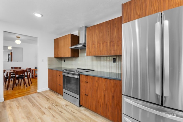 kitchen featuring dark countertops, stainless steel appliances, wall chimney exhaust hood, brown cabinetry, and decorative backsplash