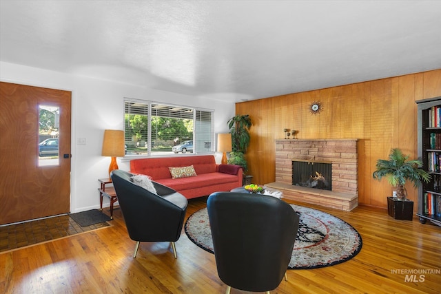 living area featuring a stone fireplace, wood finished floors, baseboards, and wood walls