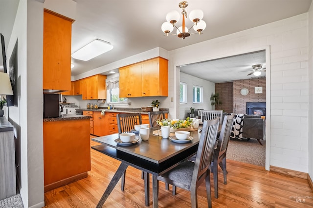 dining space featuring a wood stove, ceiling fan with notable chandelier, sink, light hardwood / wood-style flooring, and brick wall