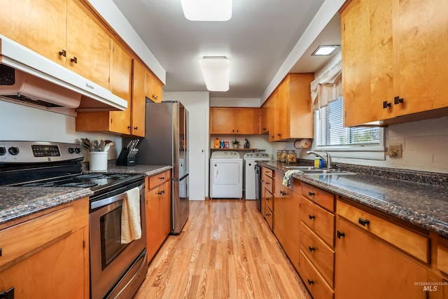 kitchen featuring sink, dark stone countertops, washing machine and dryer, light wood-type flooring, and stainless steel appliances