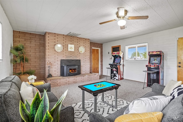 living room featuring a wood stove, ceiling fan, carpet floors, and brick wall