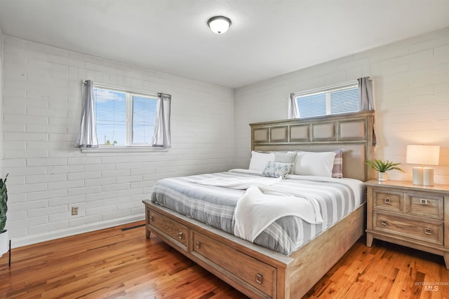 bedroom featuring light hardwood / wood-style floors, multiple windows, and brick wall