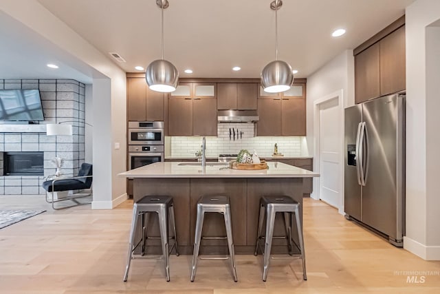 kitchen featuring sink, stainless steel appliances, light hardwood / wood-style flooring, pendant lighting, and a breakfast bar area