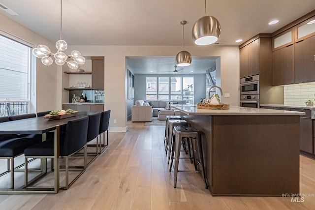 kitchen with a kitchen breakfast bar, decorative light fixtures, light hardwood / wood-style flooring, and an island with sink