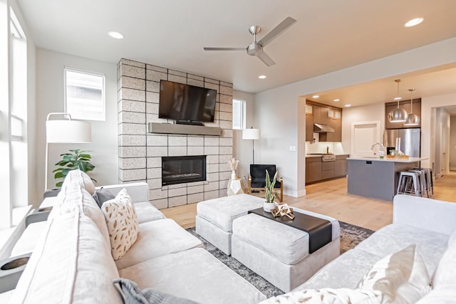 living room with ceiling fan, sink, a fireplace, and light hardwood / wood-style flooring