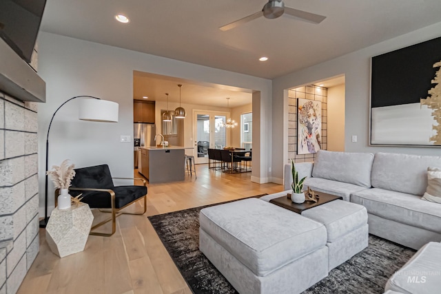 living room featuring light hardwood / wood-style flooring, ceiling fan with notable chandelier, and sink