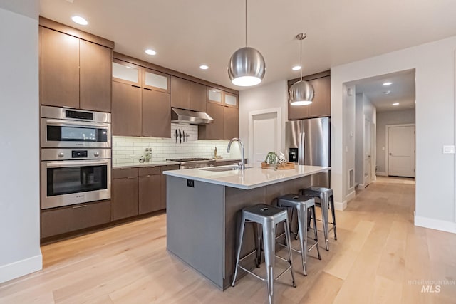 kitchen featuring sink, appliances with stainless steel finishes, tasteful backsplash, decorative light fixtures, and light hardwood / wood-style floors