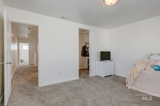 unfurnished bedroom with a walk in closet, visible vents, carpet floors, and a textured ceiling