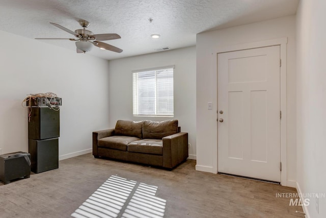 living area with a ceiling fan, visible vents, wood finished floors, baseboards, and a textured ceiling