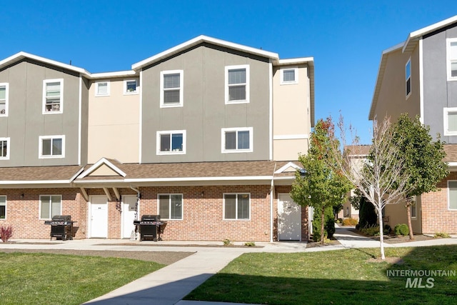 view of front facade with a front yard, stucco siding, brick siding, and a shingled roof