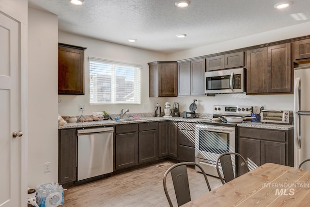 kitchen with light wood finished floors, dark brown cabinets, appliances with stainless steel finishes, and a textured ceiling