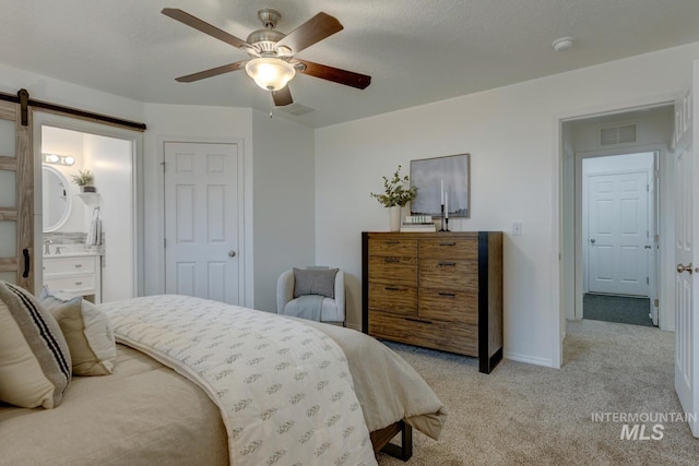 bedroom with ceiling fan, a barn door, a textured ceiling, connected bathroom, and light colored carpet