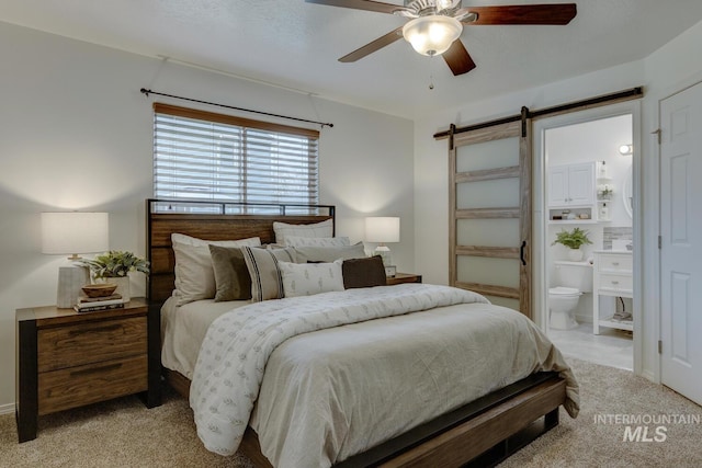 bedroom with ceiling fan, a barn door, light carpet, and connected bathroom